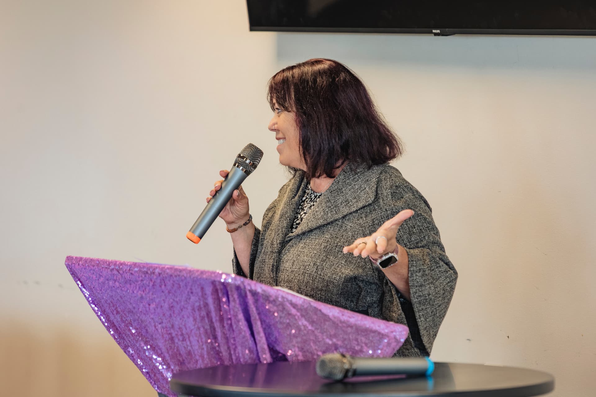 Beth Ali smiling warmly while speaking with a microphone on stage