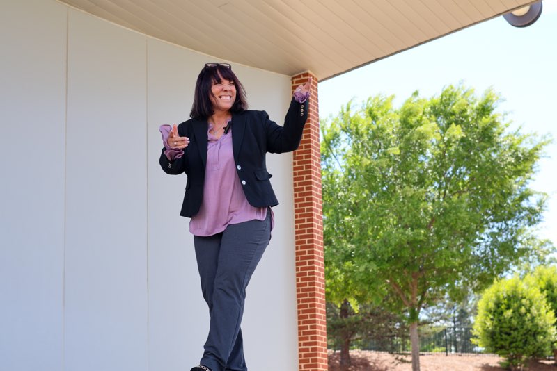 Beth Ali laughing with arms open on a sunlit porch